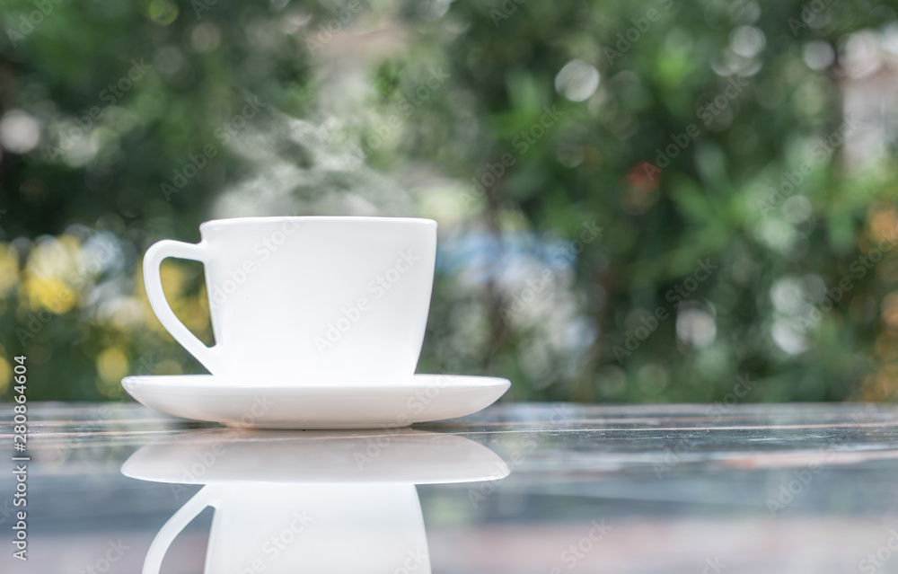 A cup of hot coffee in white cup with steaming at garden in coffee shop A cup of hot coffee in white cup with steaming at garden in coffee shop