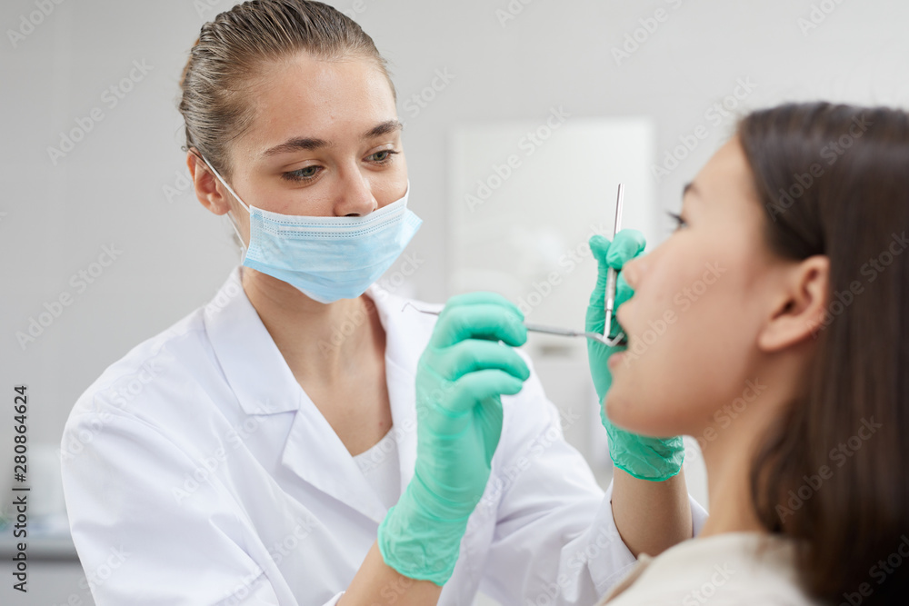 Portrait of young female dentist wearing protective mask while examining patient in clinic, copy space