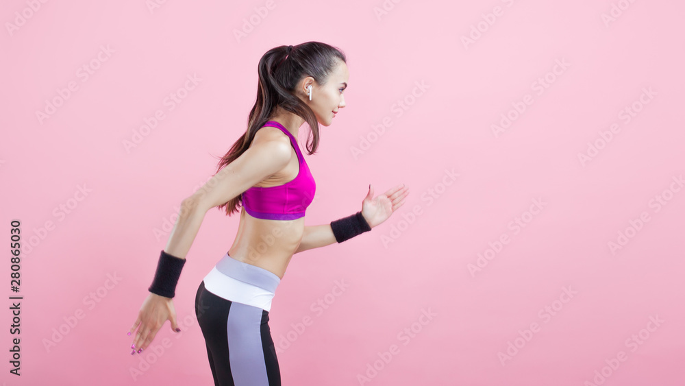 A young attractive girl runs with smile, wireless headphones and in a bright sports top, on a pink background, cardio. A young attractive girl runs with smile, wireless headphones and in a bright sports top, on a pink background, cardio.