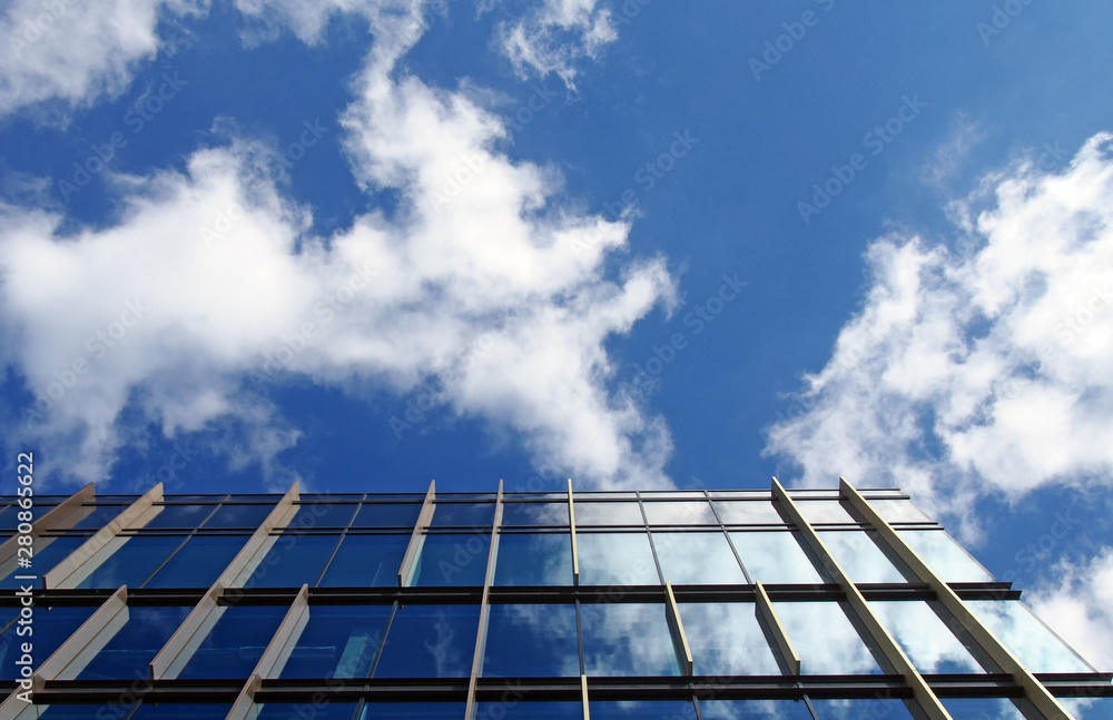 modern office building with mirrored glass windows reflecting a bright blue sky and white clouds modern office building with mirrored glass windows reflecting a bright blue sky and white clouds