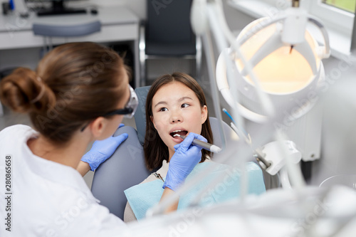 High angle portrait of female dentist performing medical procedure on Asian girl  copy space