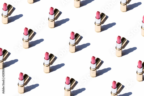 Seamless pattern of open pink tinted lipstick in gold case flat lay on white ...