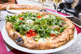 Italian pizza with arugula, tomato and cheese on the table in a restaurant outside over blurred background