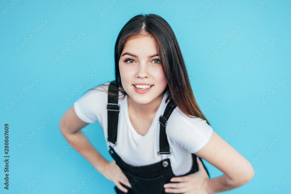 Charming smiling girl with dark long hair in white t-shirt isolated on blue background Charming smiling girl with dark long hair in white t-shirt isolated on blue background