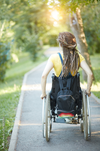 Young woman with pigtails in wheelchair outdoors, back view photo, free time, spare time, lifestyle. full length photo