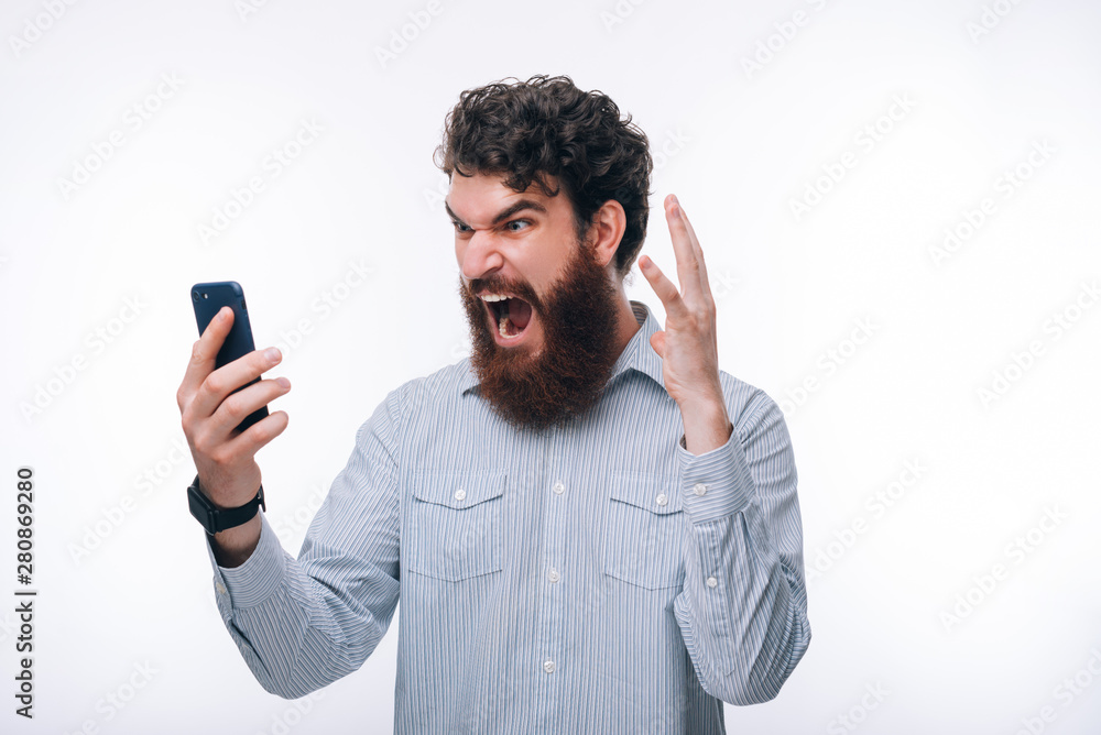 Photo af angry man in casual screaming and looking at smartphone Photo af angry man in casual screaming and looking at smartphone