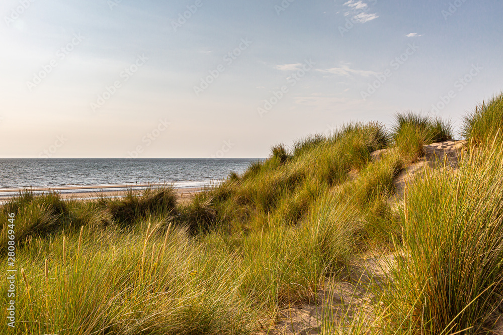 Looking out over marram grass covered sand dunes towards the beach and the ocean, at Formby in Merseyside