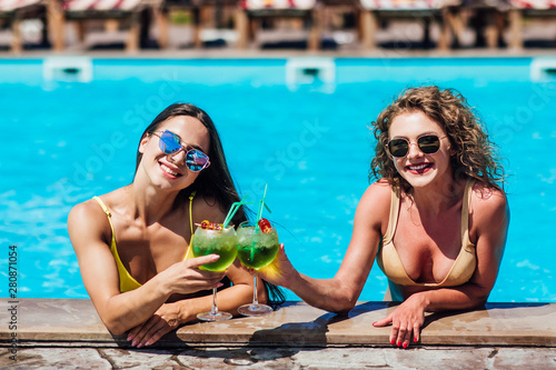 Two beautiful women relaxing in swimming pool with cocktails. © Тарас Нагирняк