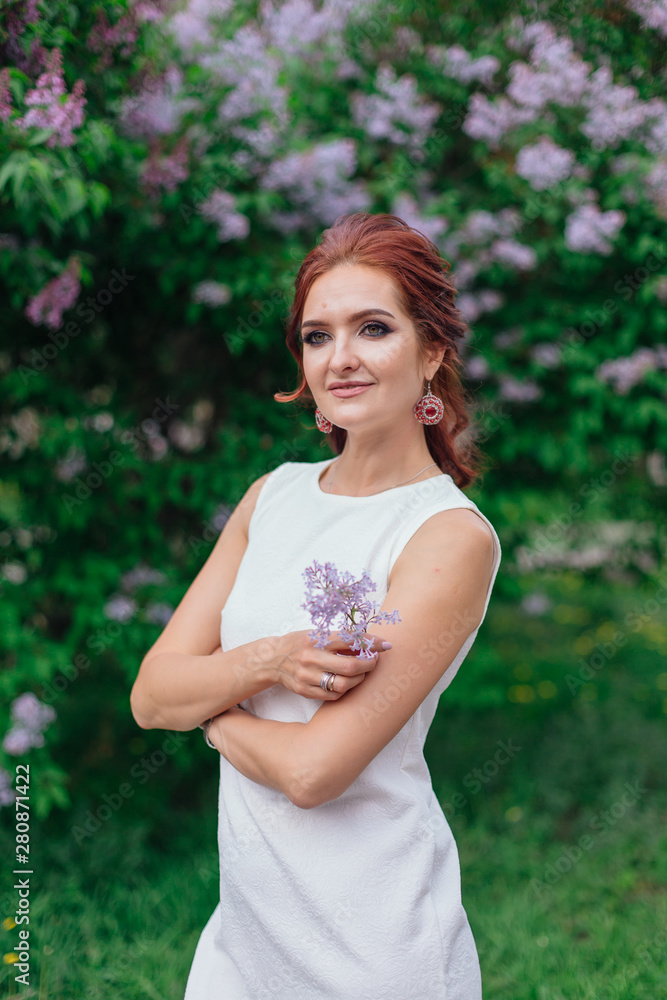 Charming woman wearing beautiful white dress standing next to lilac bush Charming woman wearing beautiful white dress standing next to lilac bush