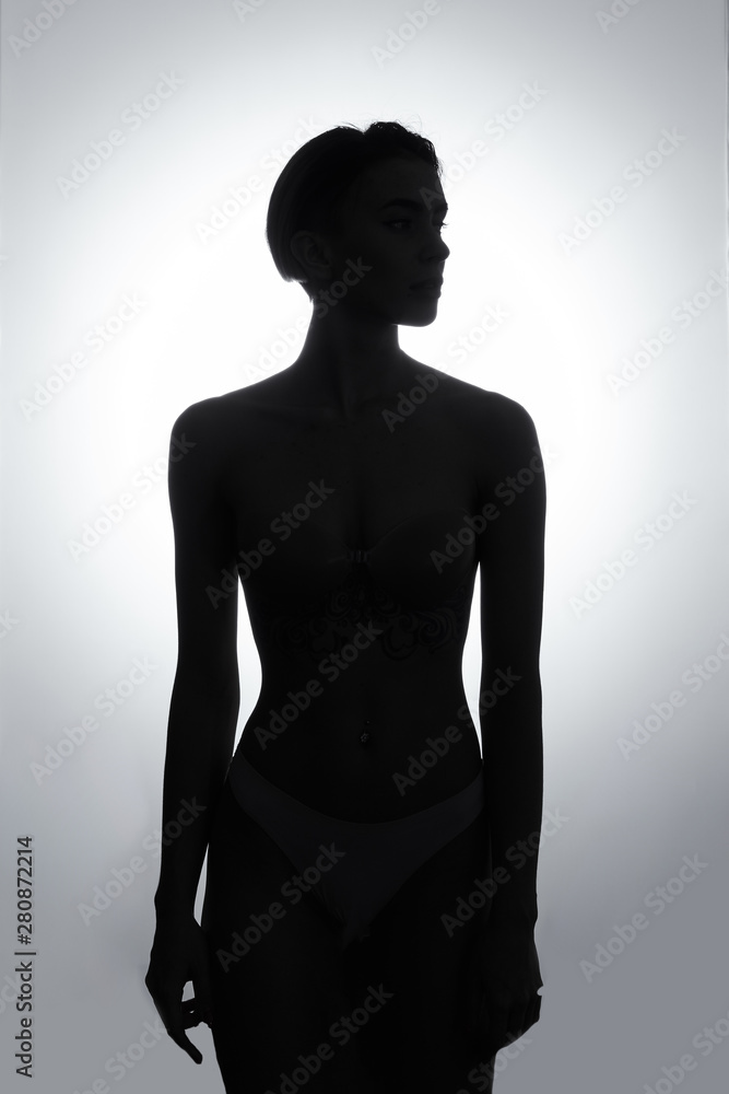 Fototapeta premium Black and white silhouette of young, sporty girl in stylish white lingerie. loneliness concept. isolated white background