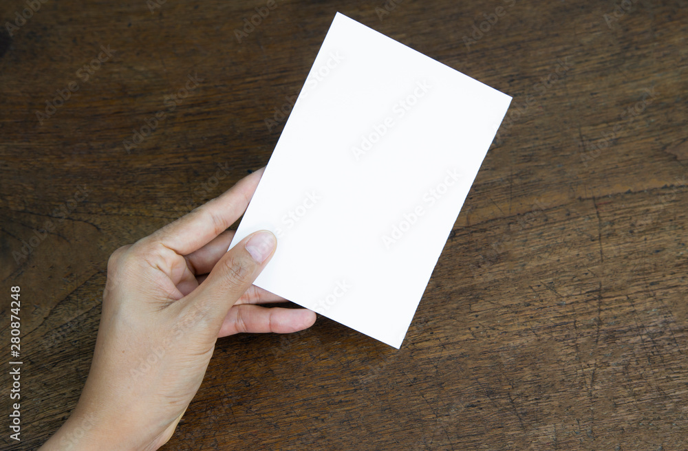 Obraz premium A6 Flyer / Postcard / Invitation Mock-Up - hands holding a blank flyer on a on a wooden table background.