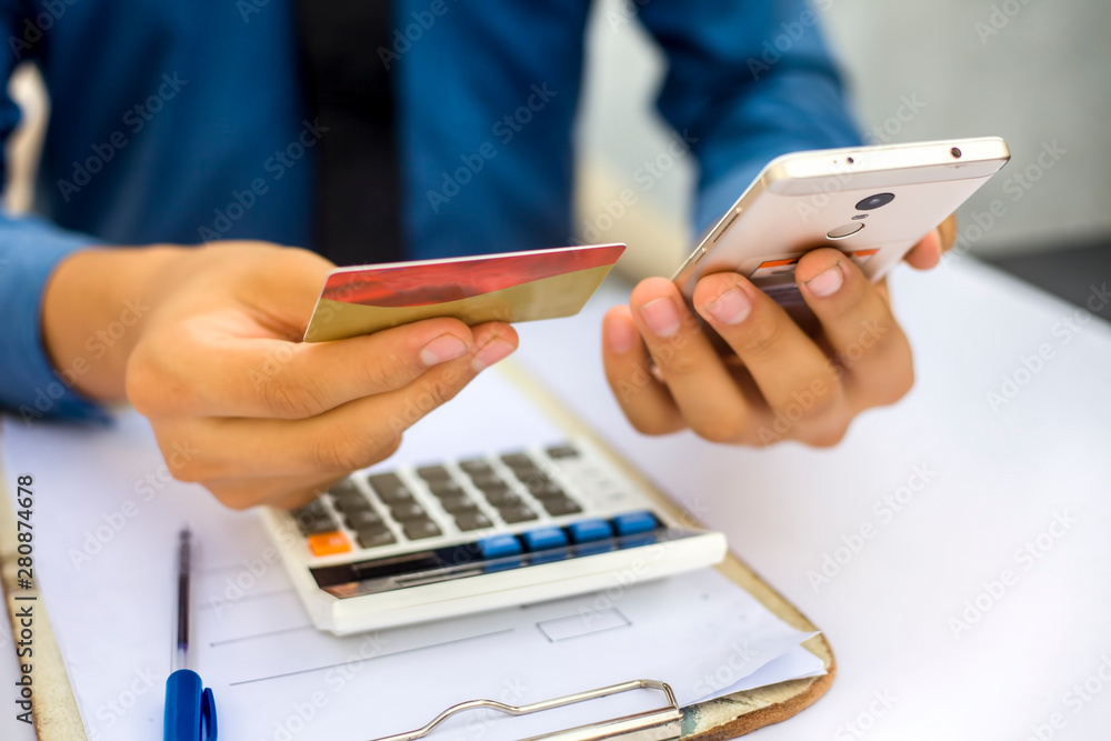 Fototapeta premium Close up of employee holding a smart cell phone and credit card in his hand wearing a blue colored shirt and black necktie. Concept of banking and shopping isolated on white.