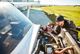 young handsome father and his little son in aviator glasses trying to fix electrical wire system of light propeller aircraft, using special instruments, doing repair works near hangar.