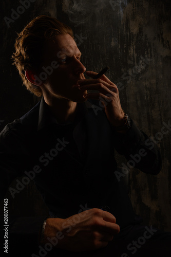 Confident casual young man and smoking cigarette. Studio portrait against dark background.