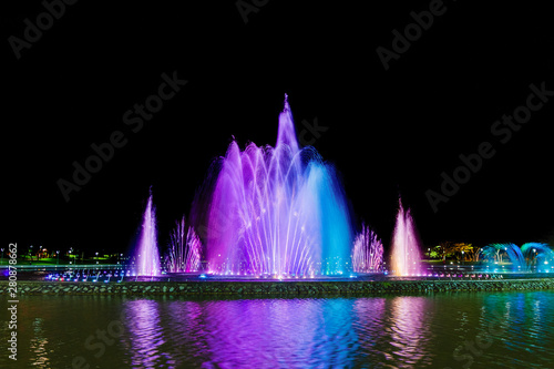 Colorful luminous and musical fountain. Night view. Multicolored streams of water are blurred against a black sky.