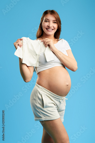 charming ositive girl choosing, selecting clothes for her baby. isolated blue background. studio shot. sale, trade photo