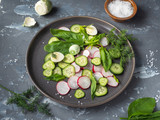 Light vegetable appetizer of cucumbers, radishes and spinach on a kurglova plate, eggs and saltcellar with coarse salt