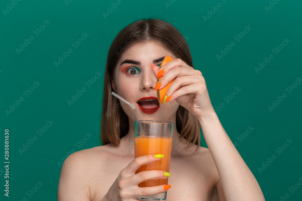 Closeup portrait of beautiful young woman with bright color make-up squeezing orange juice out of a an orange half Closeup portrait of beautiful young woman with bright color make-up squeezing orange juice out of a an orange half