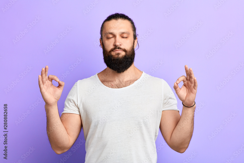 Fototapeta premium handsome relaxed young man, with closed eyes , in meditation zen mode, isolated blue background. Stress relief techniques. close up portrait. man reducing stress. hobby, lifestyle, free time