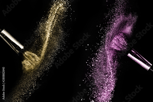 Cosmetic brush with purple and golden cosmetic powder spreading for makeup artist and graphic design in black background