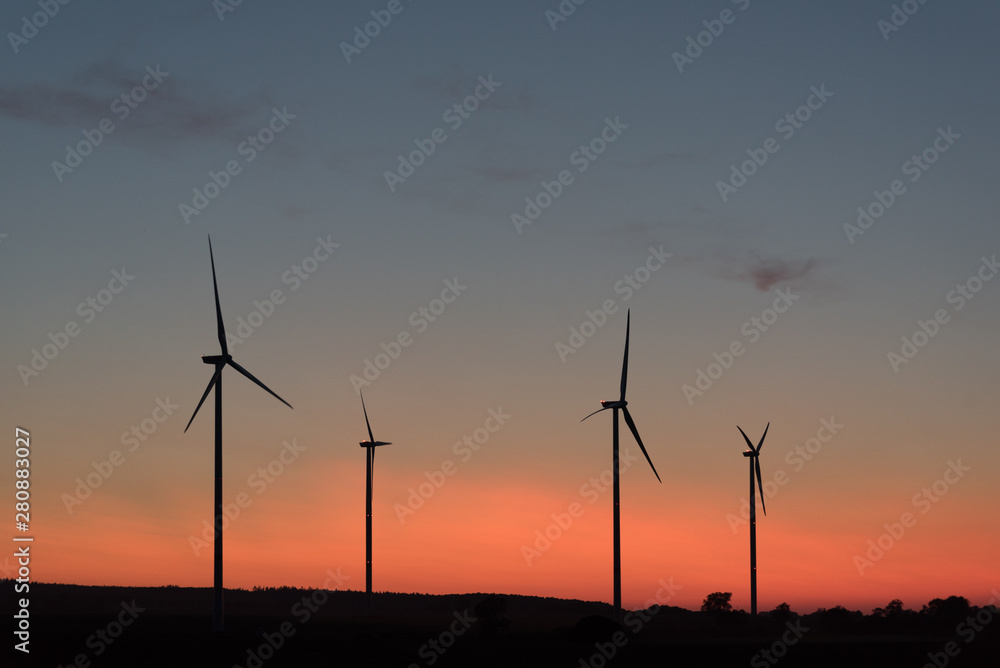 Four wind generators in the evening light, orange and blue sky, silhouette