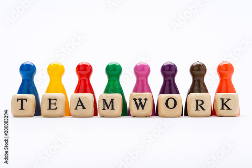 Word teamwork written on wooden blocks with pawns in various colors on white background, as a concept of success and diversity