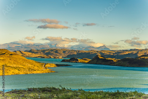 Beautiful panoramic view of blue water lake with golden yellow grass with background of nature mountains range with cloud in autumn, Torres del Paine national park, south Patagonia, Chile