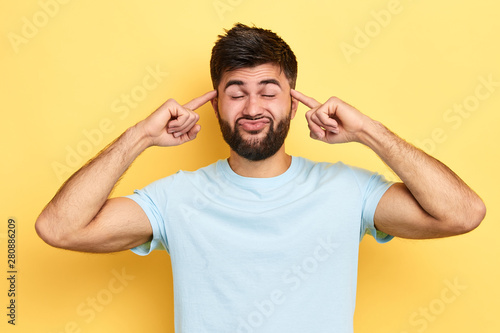 funny man making faces, holding fingers on temples. close up portrat, guy having fun.isolated yellow background, © the faces