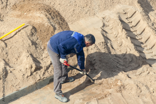 Worker with a shovel digging sand.