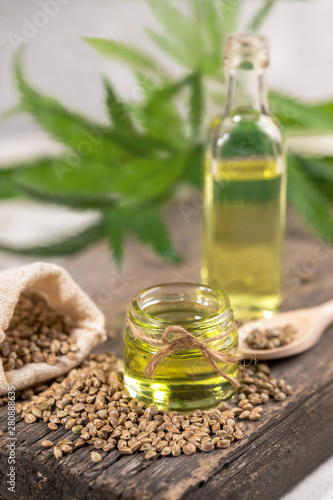 CBD oil.  Hemp oil in two glass jar and bottle with grain in the sack on wooden board with leaves of cannabis on background.