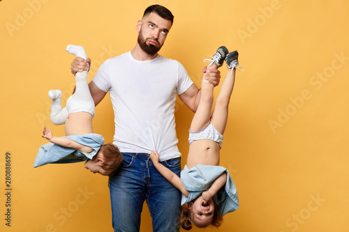 Exhausted daddy holding his children upside down, being tired of playing with children. close up photo. isolated yellow background.I need a rest. exhaustion concept photo