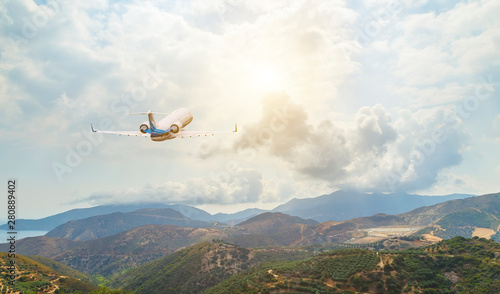White passenger plane in flight. The plane flies against a background of mountain landscape. Aircraft rear view.