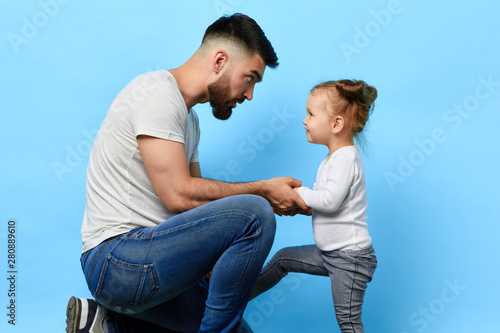 caring father and little obedient daughter who listens to the instruction of parent on blue isolated background. daddy making an observation to kid. dad asking daughter to behave well photo