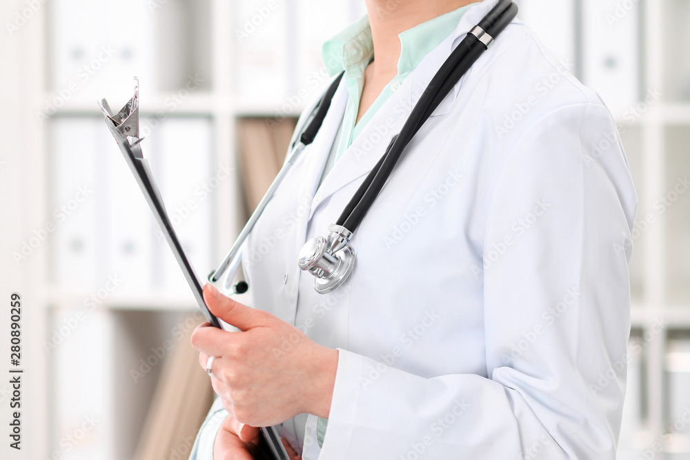 Stethoscope at female doctor breast at hospital office. Unknown physician's hands close-up. Green tone of blouse. Medicine and health care concept Stethoscope at female doctor breast at hospital office. Unknown physician's hands close-up. Green tone of blouse. Medicine and health care concept