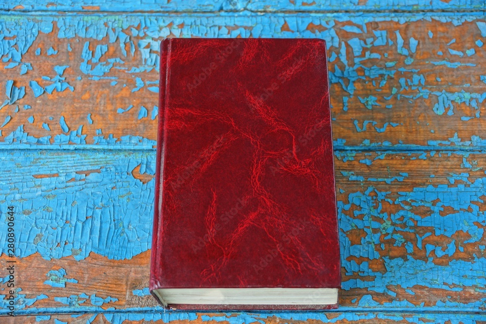  closed book with a red cover is lying on a blue brown worn table