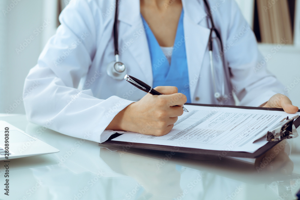Doctor woman filling up medical form while sitting at the table, close-up of hands Doctor woman filling up medical form while sitting at the table, close-up of hands