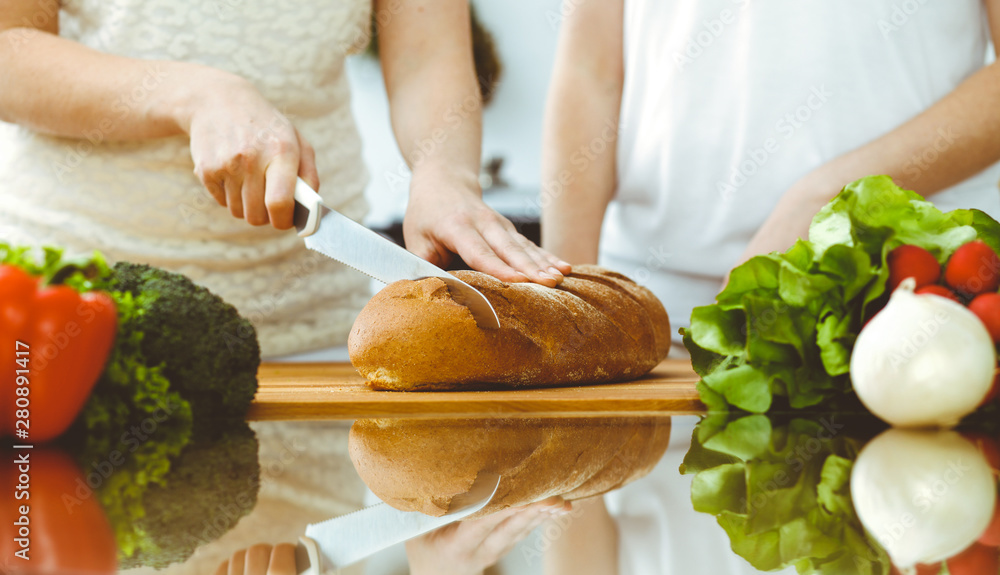 Closeup of human hands cooking in kitchen. Mother and daughter or two female friends cutting bread for dinner. Friendship, family and lifestyle concepts Closeup of human hands cooking in kitchen. Mother and daughter or two female friends cutting bread for dinner. Friendship, family and lifestyle concepts