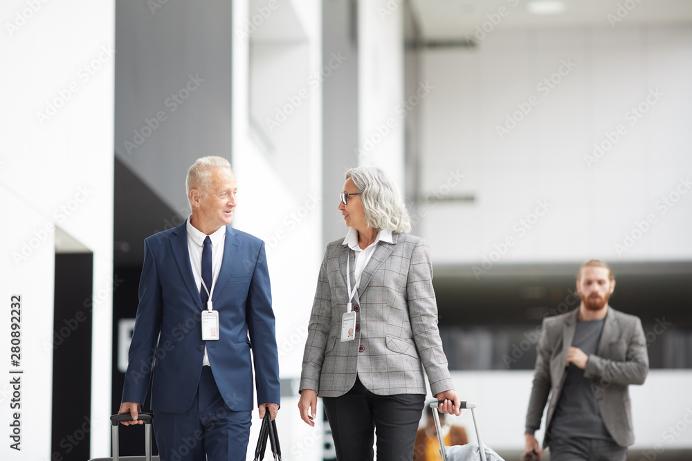 Content senior multi-ethnic business representatives with badges hanging on necks carrying bags and talking while going for boarding Content senior multi-ethnic business representatives with badges hanging on necks carrying bags and talking while going for boarding