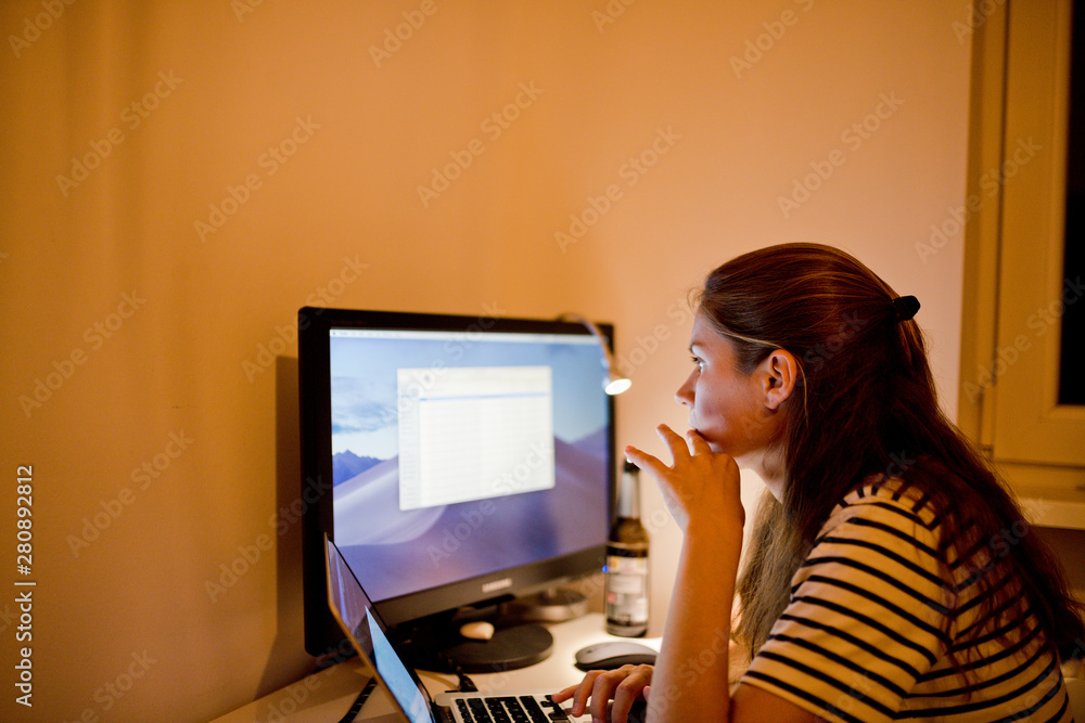 Frau denkt über ein Projekt nach und sitzt vor ihrem Laptop und Monitor Frau denkt über ein Projekt nach und sitzt vor ihrem Laptop und Monitor