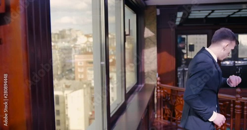 Wallpaper Mural A blond man in a tuxedo approaches the window and ponders, enjoys the panorama, looks at his watch, starts to hurry. Businessman, finance, think, sunset, view, panoramic window Torontodigital.ca