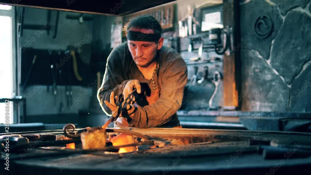 A blacksmith heats a knife on coal, holding it with tongs. A blacksmith heats a knife on coal, holding it with tongs.