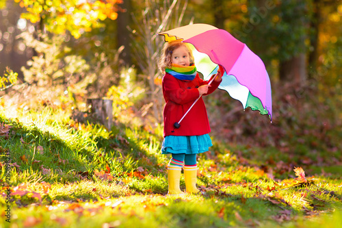 Kid with umbrella playing in autumn rain.