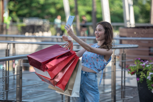Happy time to shopping concept , Asian woman holding shopping bags and selfie herself with smartphone in hands at mall centre.