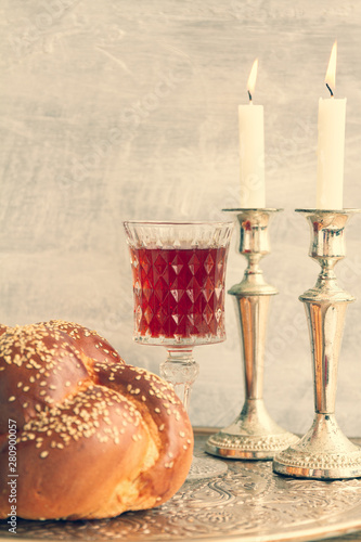 Shabbat or Sabbath kiddush ceremony composition with a traditional sweet fresh loaf of challah bread, glass of red kosher wine and candles on a vintage wood table