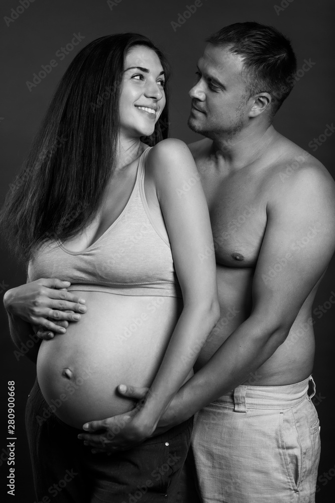 Young pregnant couple hugging and smiling. Love and tenderness. Waiting for a miracle. Black and white portrait. Vertical. Young pregnant couple hugging and smiling. Love and tenderness. Waiting for a miracle. Black and white portrait. Vertical.