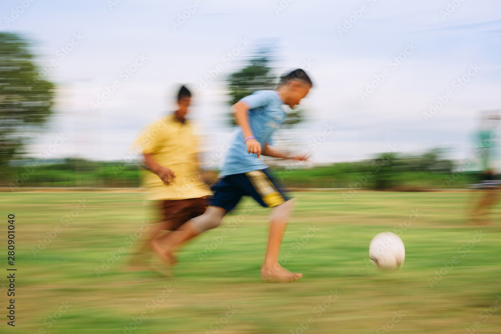 Speed motion blur picture of kids having fun playing soccer football for exercise in community rural area. Concept for sport background with anonymous people.