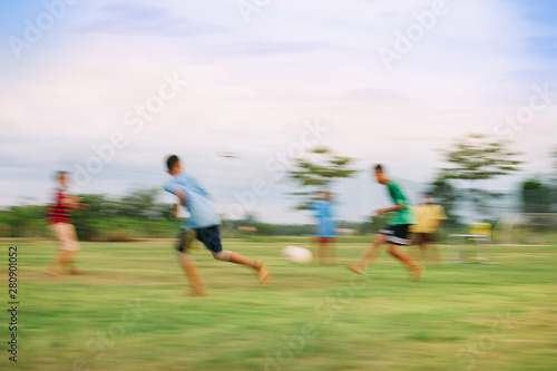 Speed motion blur picture of kids having fun playing soccer football for exercise in community rural area. Concept for sport background with anonymous people.