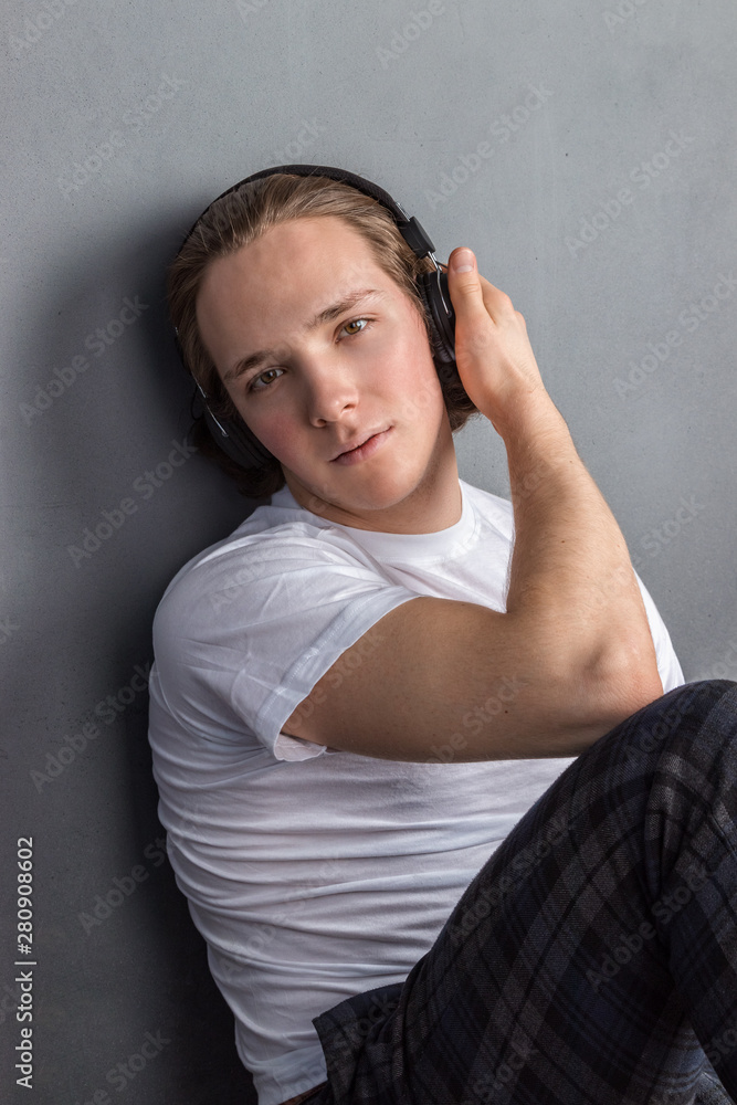 Handsome young man sitting on the floor in living room, having headphones on his head and listening music Handsome young man sitting on the floor in living room, having headphones on his head and listening music