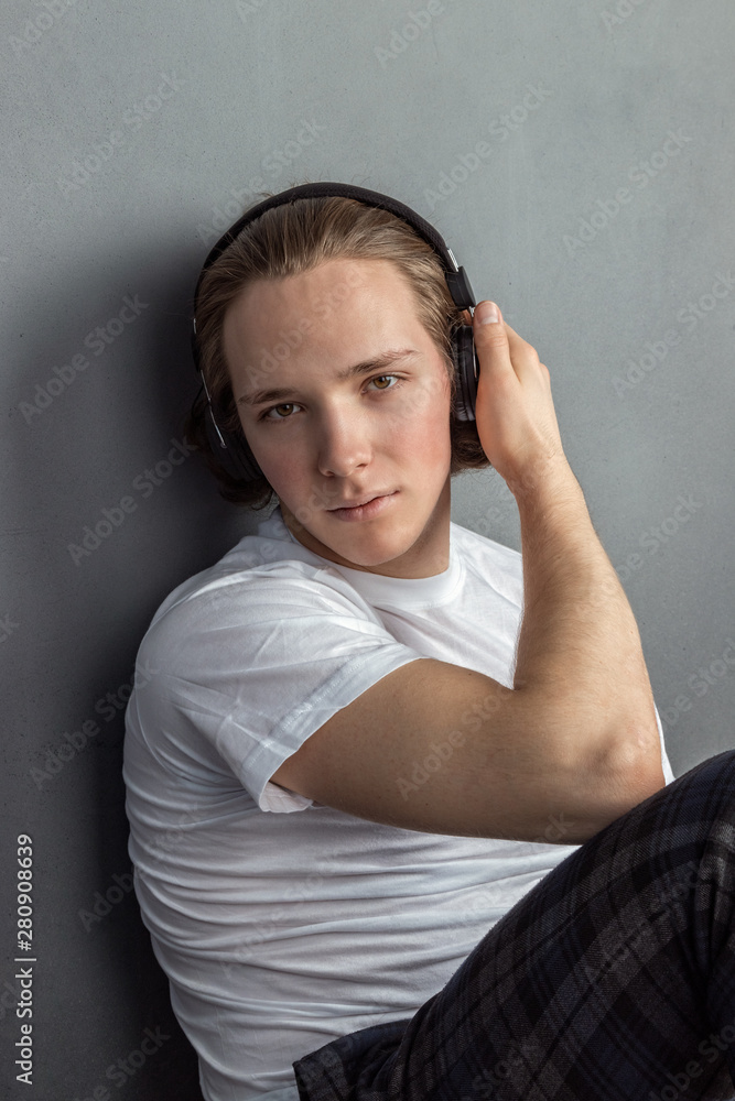 Handsome young man sitting on the floor in living room, having headphones on his head and listening music Handsome young man sitting on the floor in living room, having headphones on his head and listening music