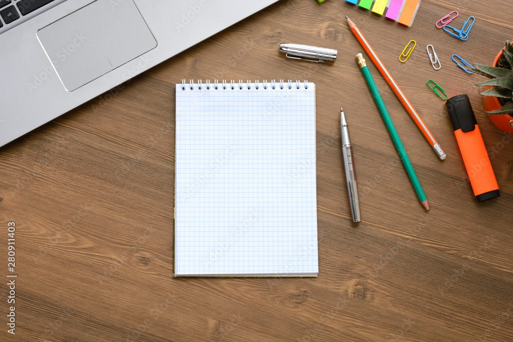 An open notebook for notes, pencils, markers, a pen, a pot with cactus, a notebook and paper clips on a wooden background (office desk). An open notebook for notes, pencils, markers, a pen, a pot with cactus, a notebook and paper clips on a wooden background (office desk).